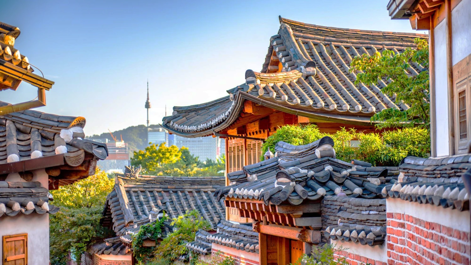 Tiled hanok rooftops on a hillside with a broadcast tower on the ridge behind