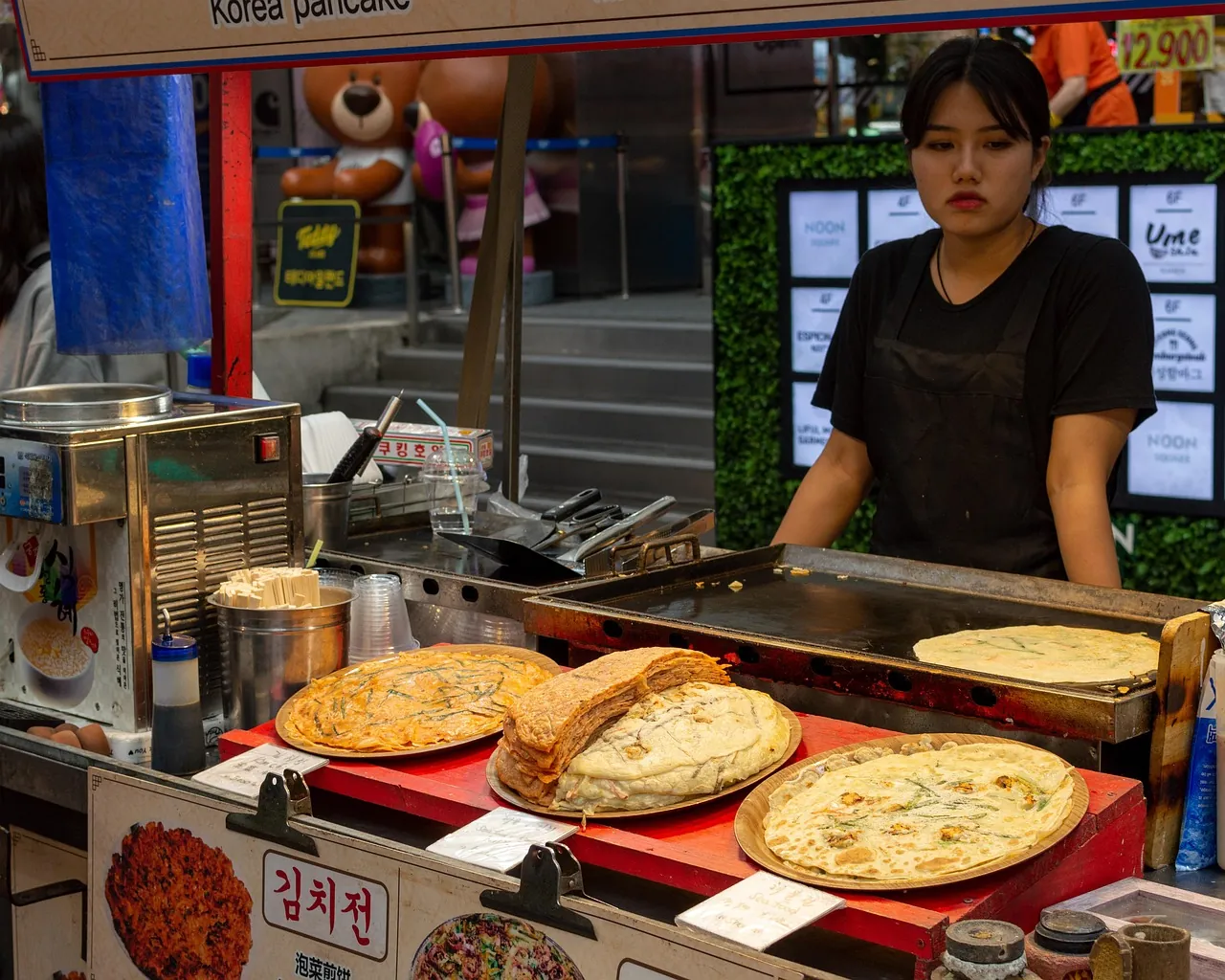 Vendor turning savoury pancakes on a griddle at a market food stall