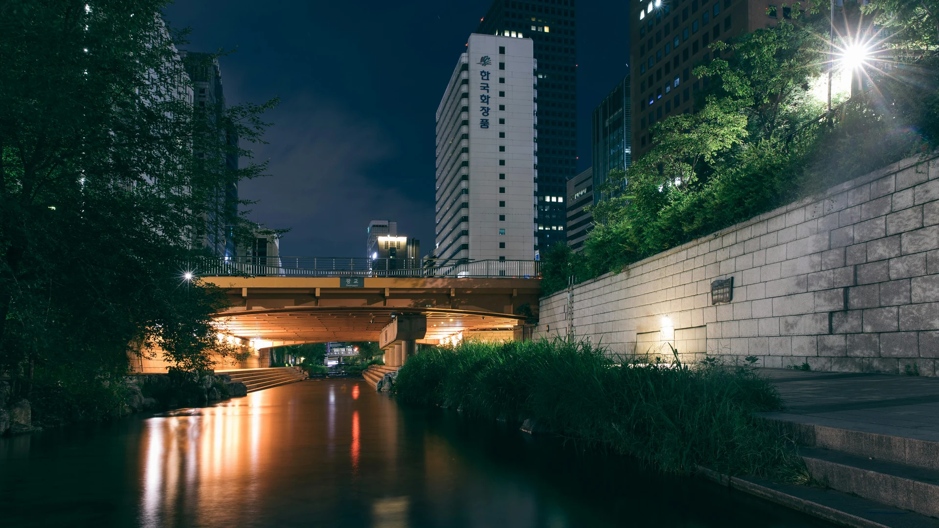 Illuminated bridge reflected on a night stream between city buildings