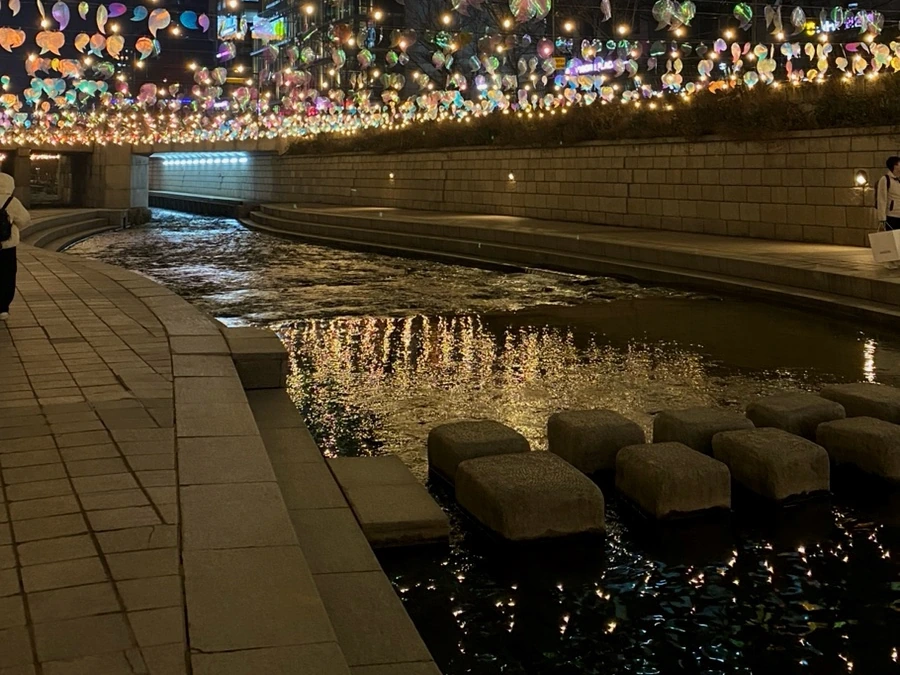 Lantern light spreading across dark water beside stepping stones