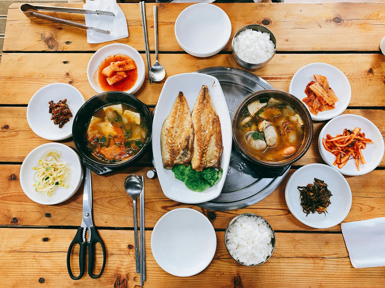 Overhead view of a Korean table with soups, grilled fish, rice and side dishes