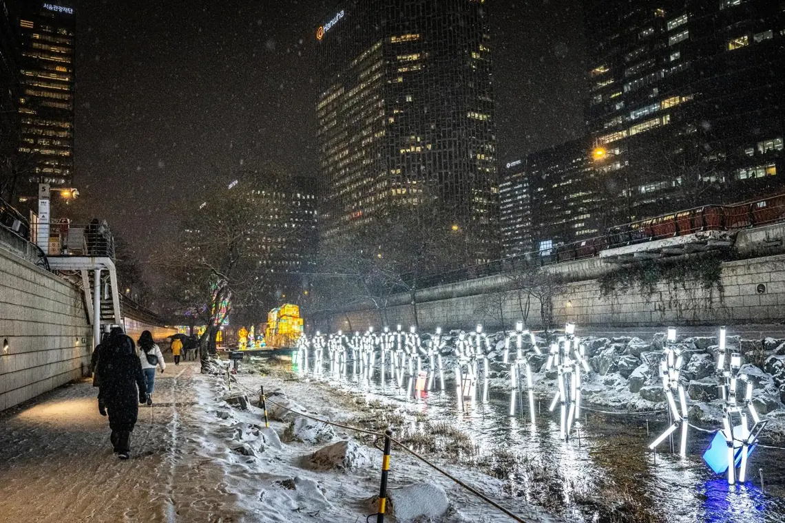Snow along a stream walkway with a white light sculpture and one passer-by