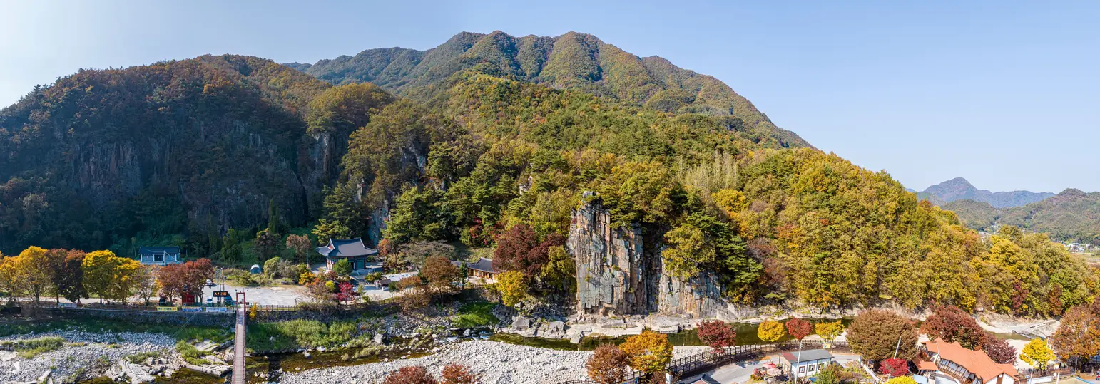 The Sainam rock face above a stony streambed in autumn