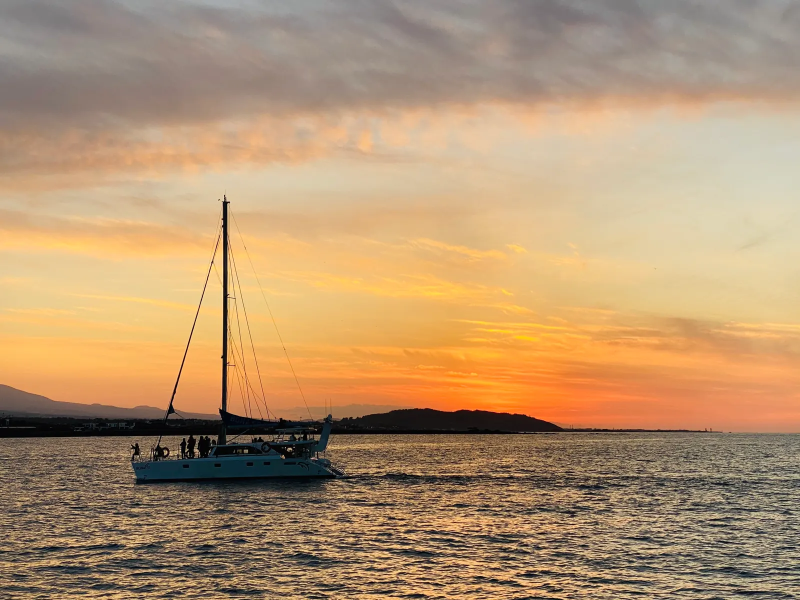 A sailing yacht silhouetted against the evening sky with a low coastline behind