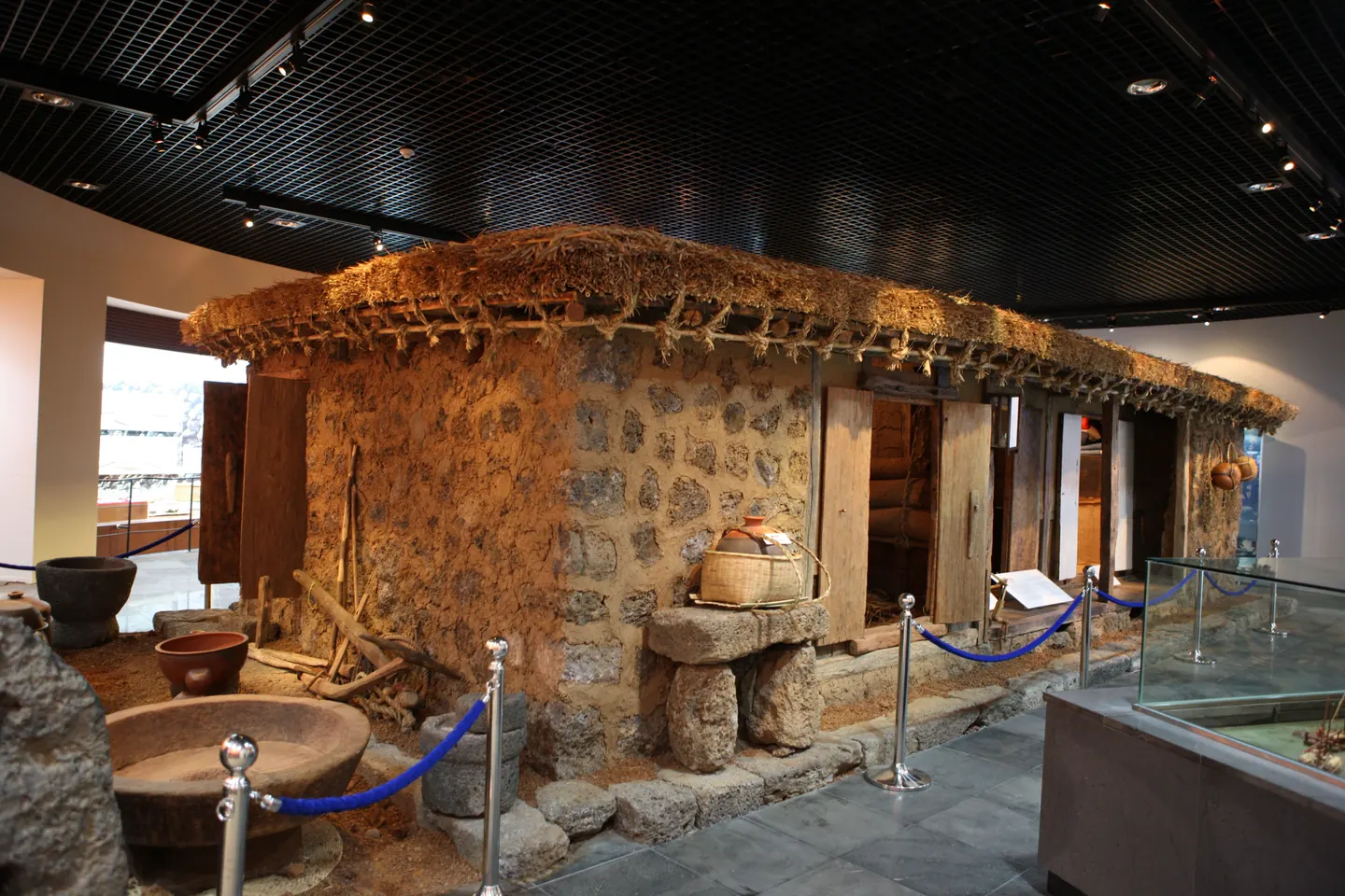 A reconstructed thatched dwelling inside a museum hall with stone mortars in front