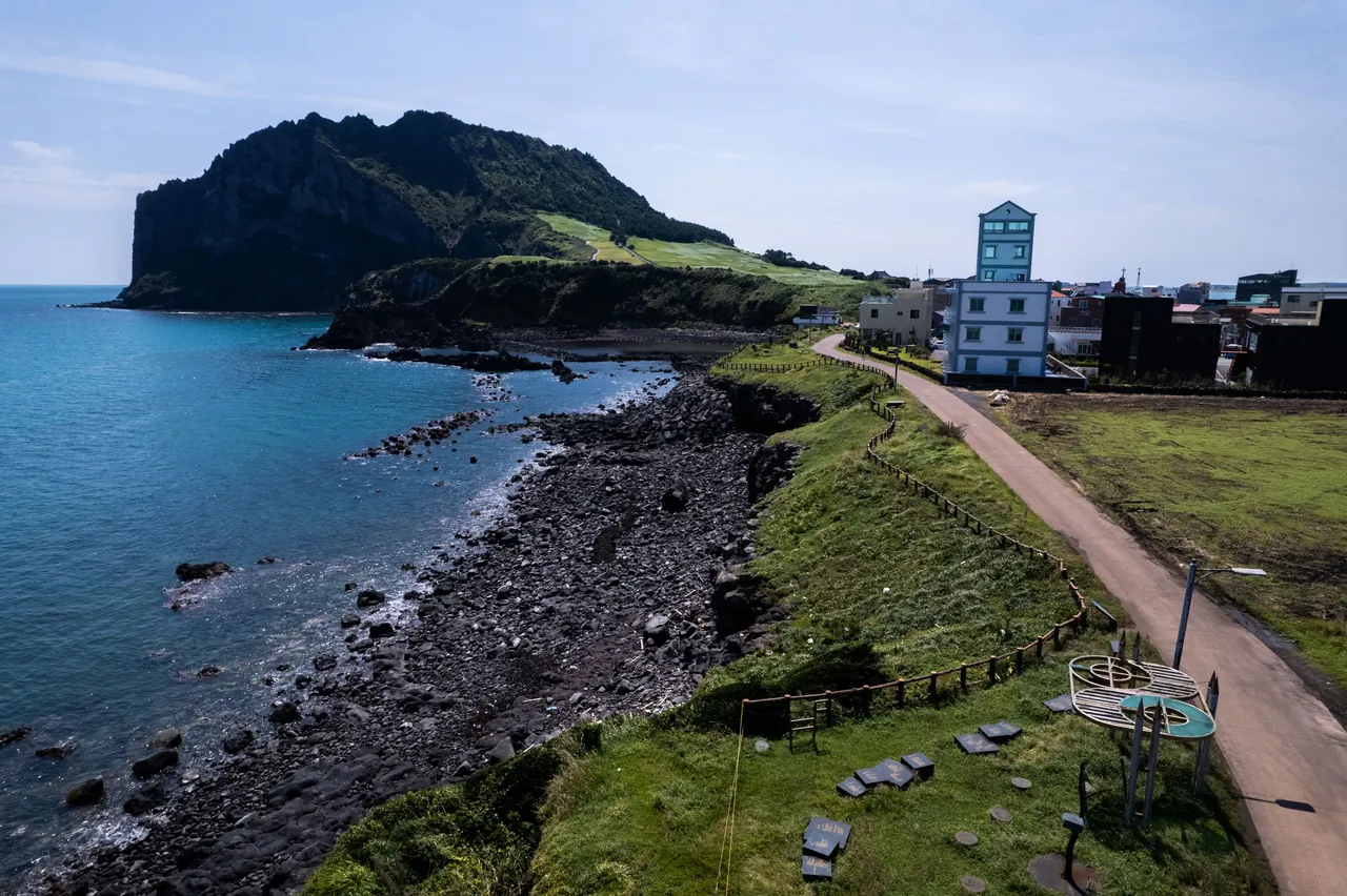 Seongsan Ilchulbong tuff cone above a black pebble shore with a fenced coastal path