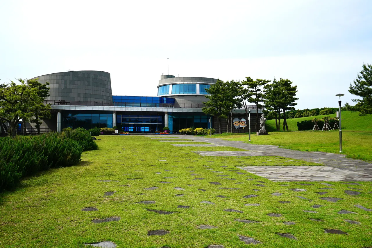The curved facade of the Haenyeo Museum above a lawn and stone paving