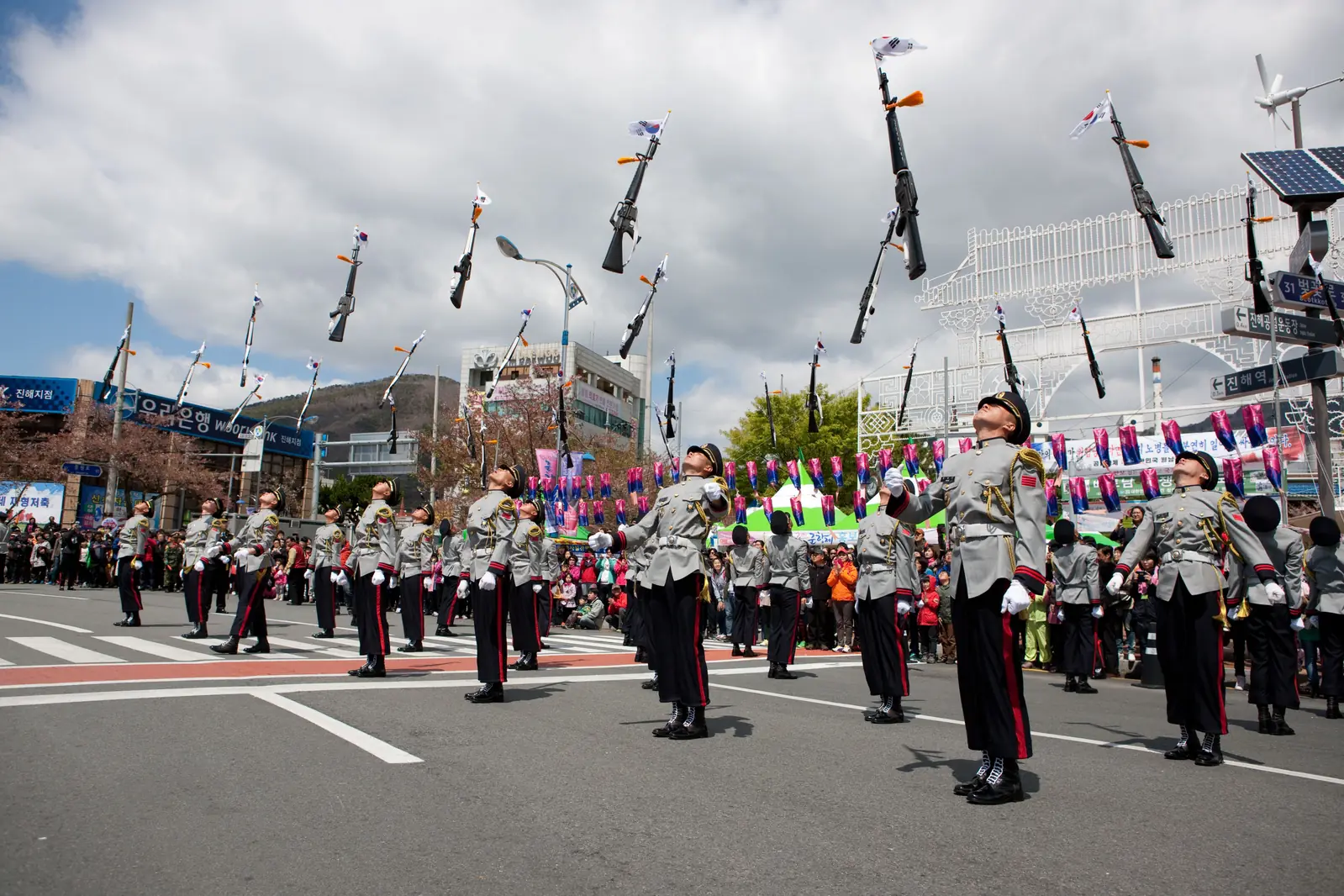 Uniformed drill team performing along a street lined with spectators
