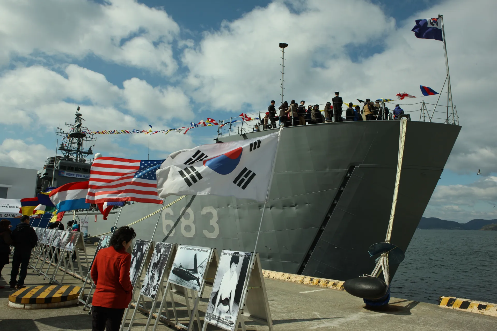 Naval ship bow with flags flying above visitors gathered on the quay
