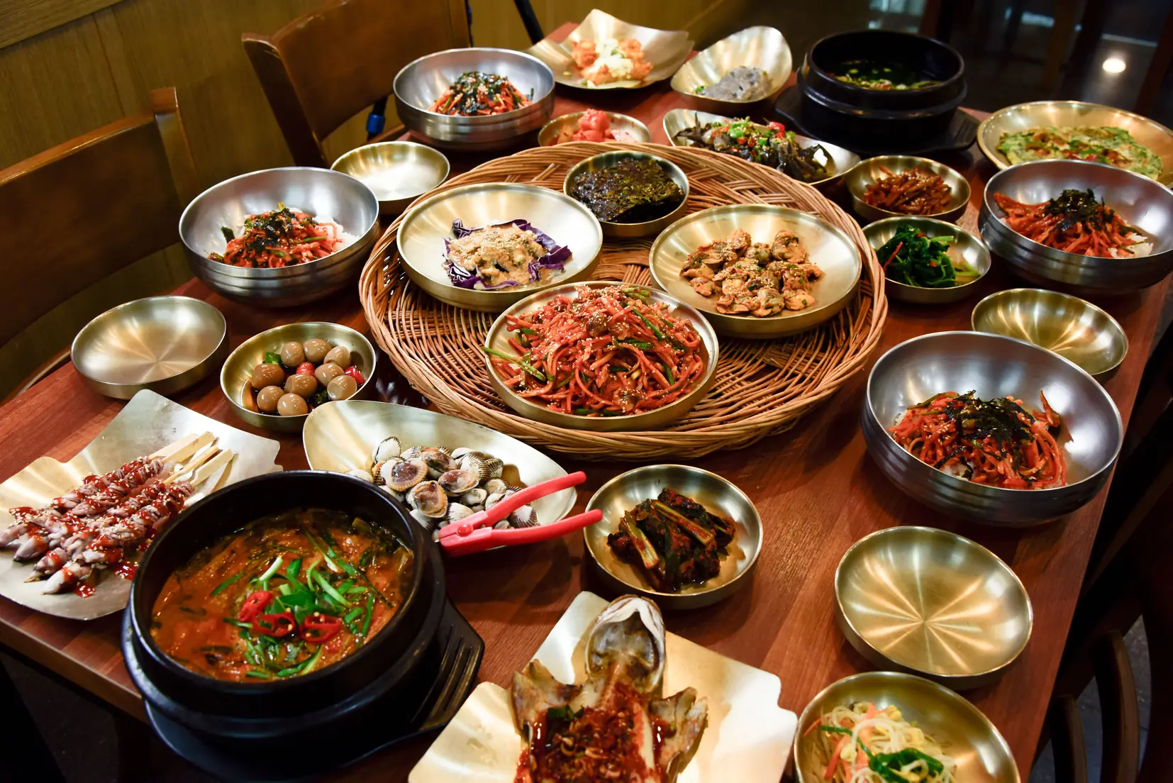 Brass bowls of side dishes covering a table around a stew and a shellfish dish
