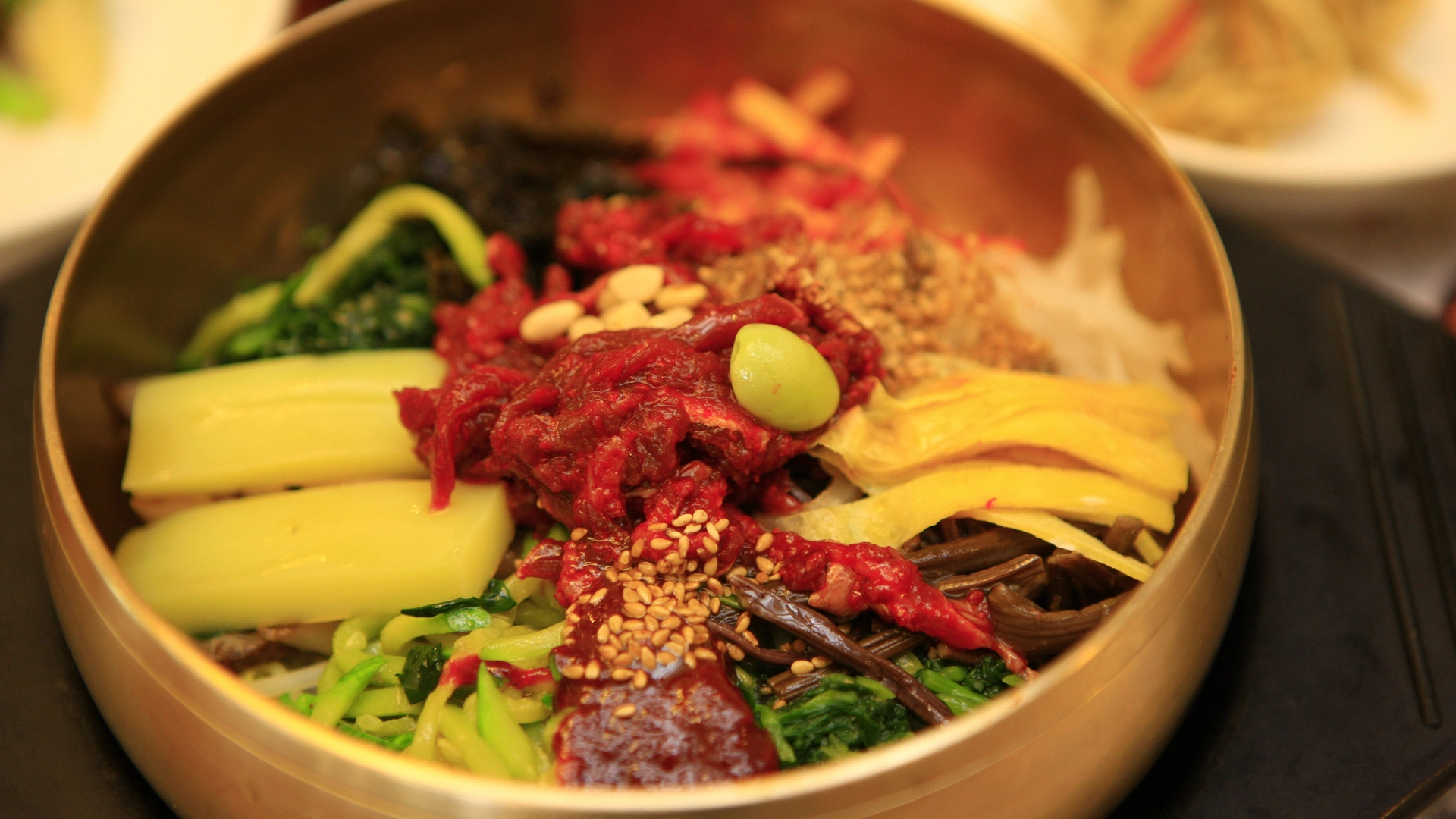 Rice topped with raw beef, vegetables, egg yolk and nuts in a brass bowl