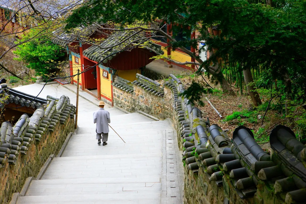 A single visitor climbing a wide stone stairway towards a red temple gate