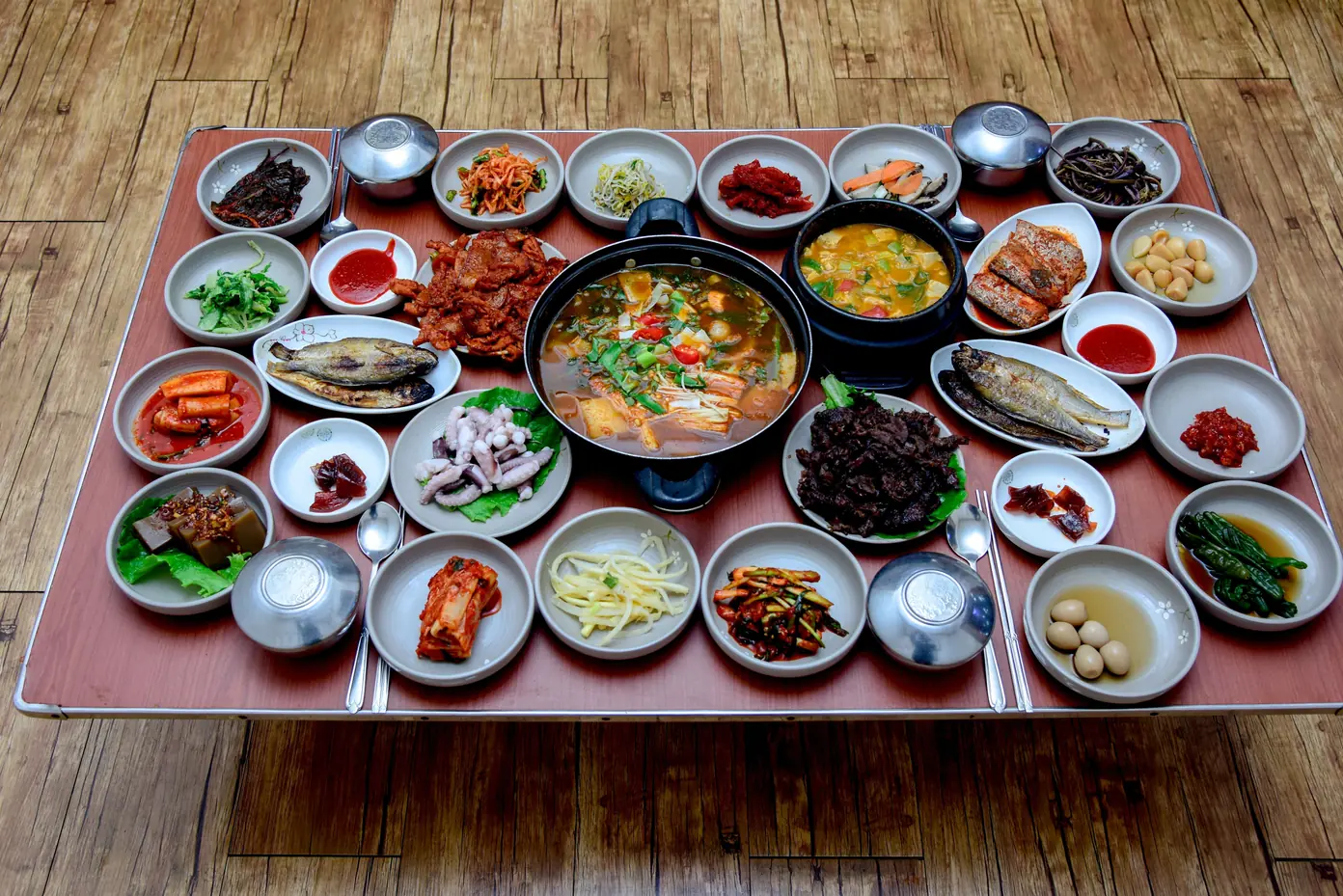 More than twenty small dishes and a shared stew pot arranged on a red table