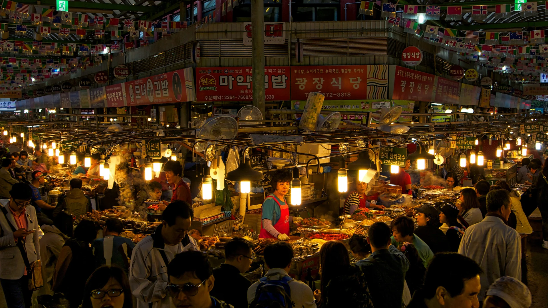 Night market alley lit by bare bulbs with stalls and shoppers on both sides