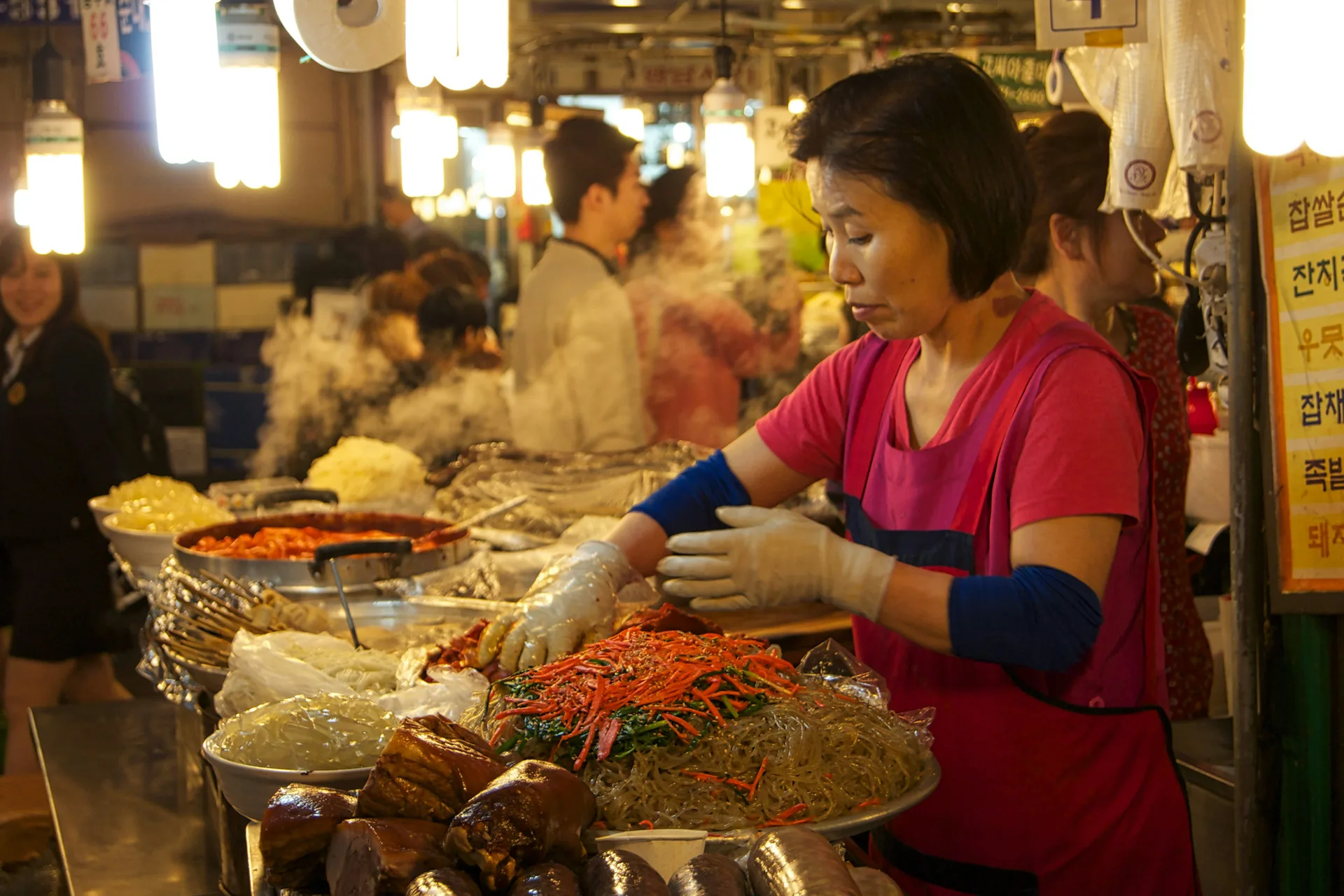 Cook in a red apron working over a steaming stall counter