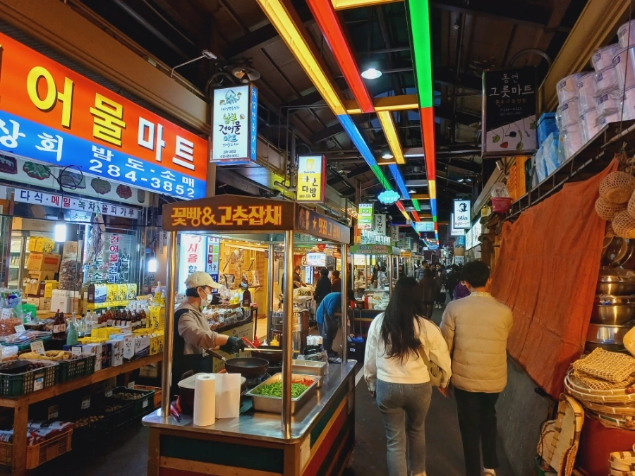 Neon shop signs above stalls in a night market lane