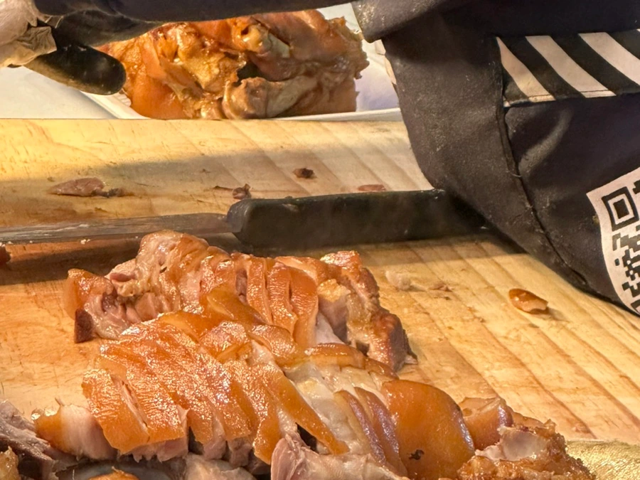 Vendor slicing braised pork on a wooden board at a market counter