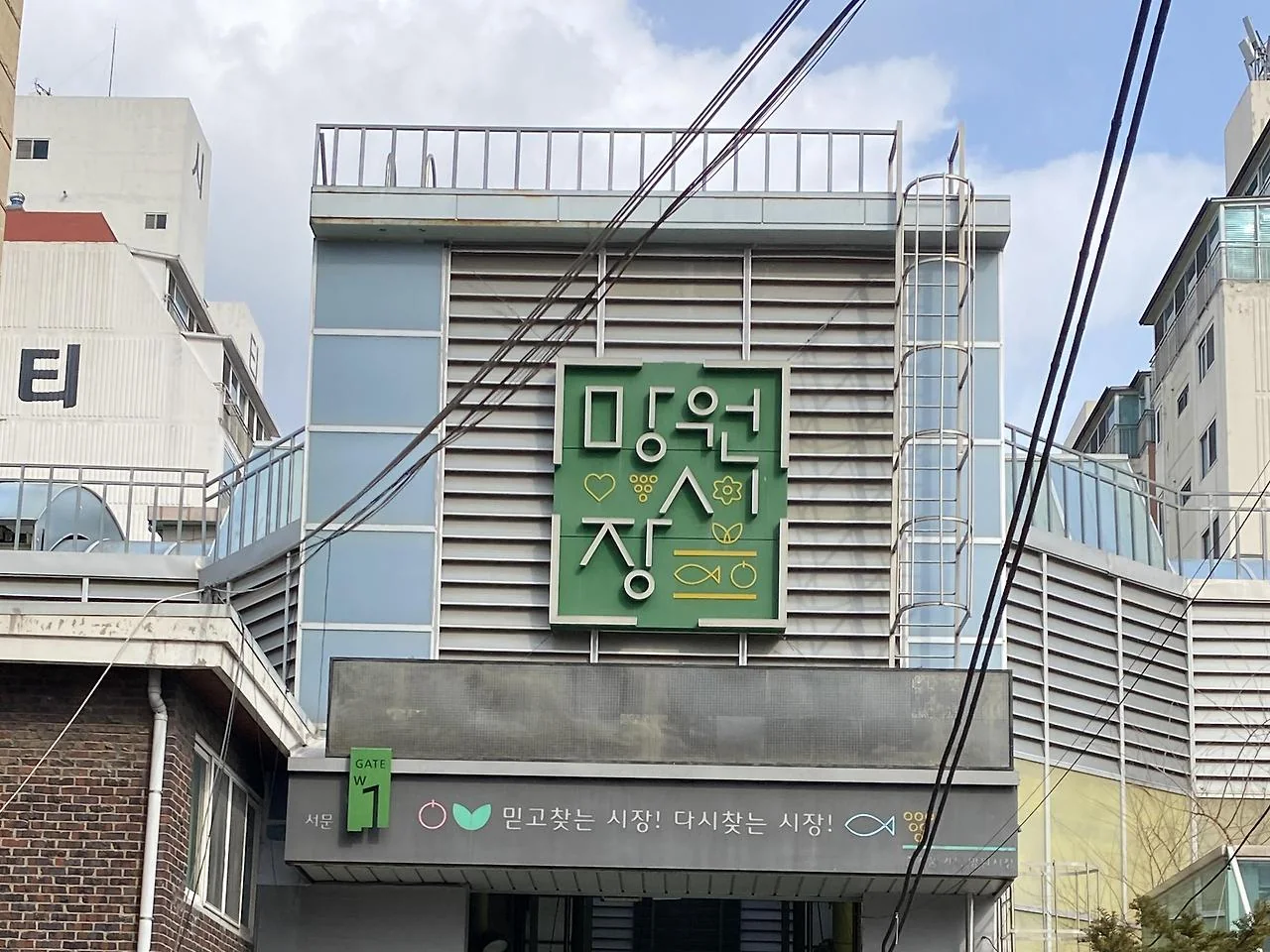 Green market gate sign above a covered entrance with shoppers walking in