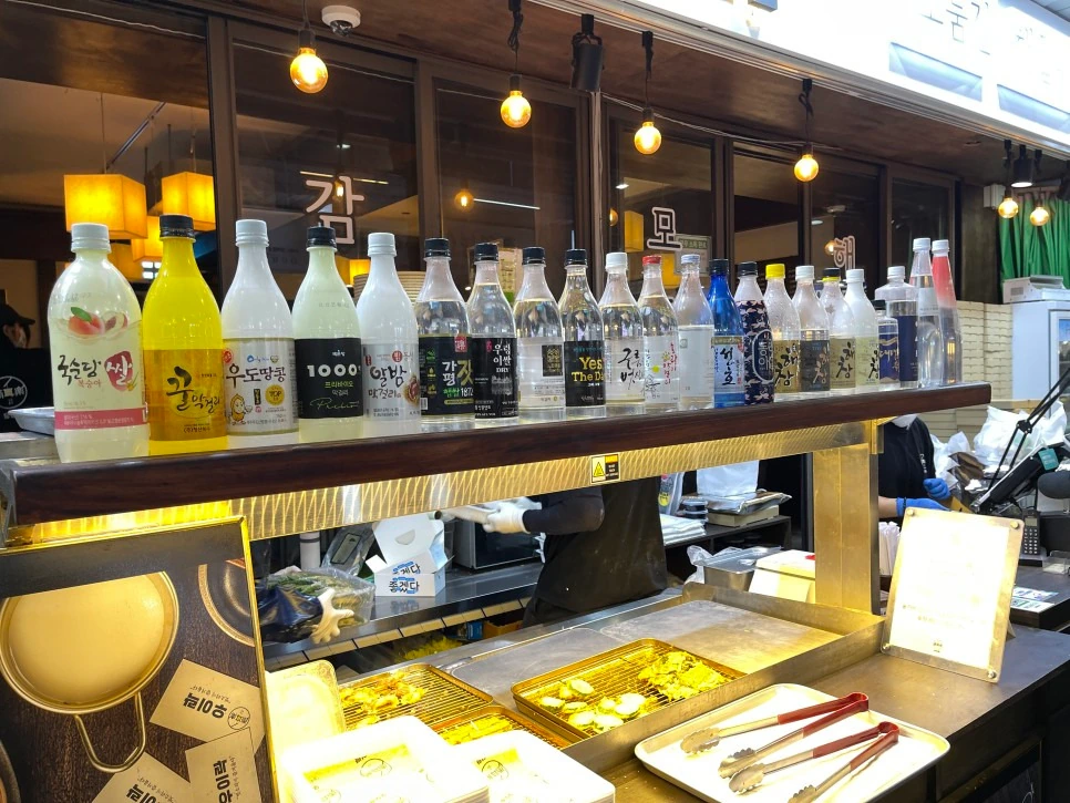 Row of rice wine and soju bottles on a shelf above a market food counter