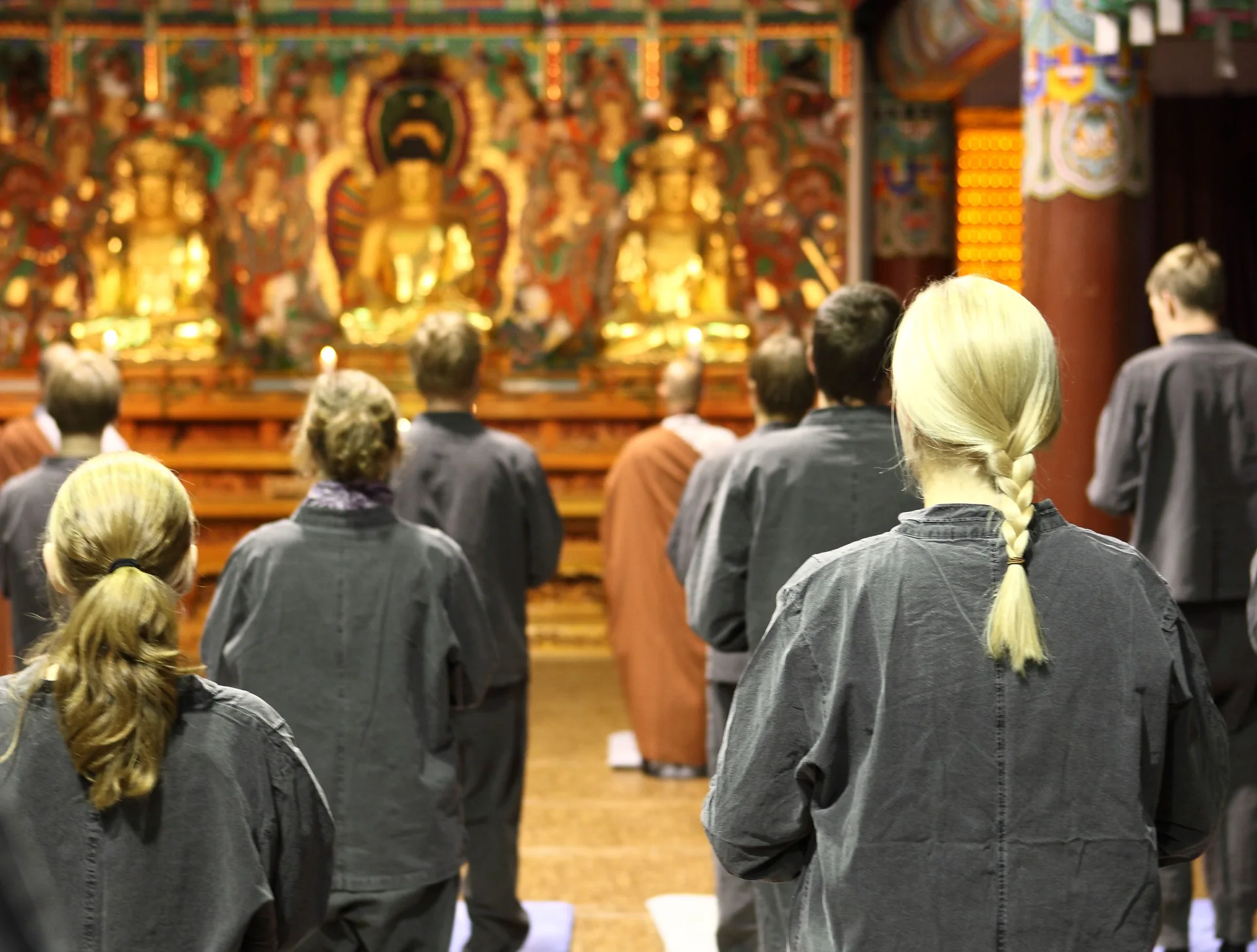 Participants in grey robes standing before a gilded altar, a robed monk facing the same direction