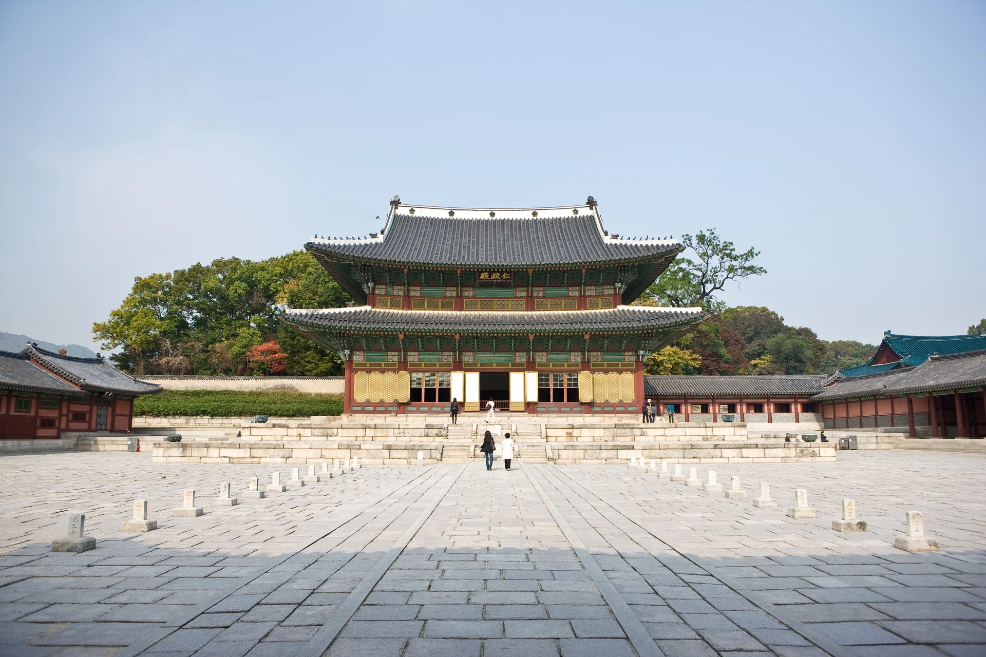 A two-tiered wooden hall facing a wide stone-paved courtyard enclosed by low corridors