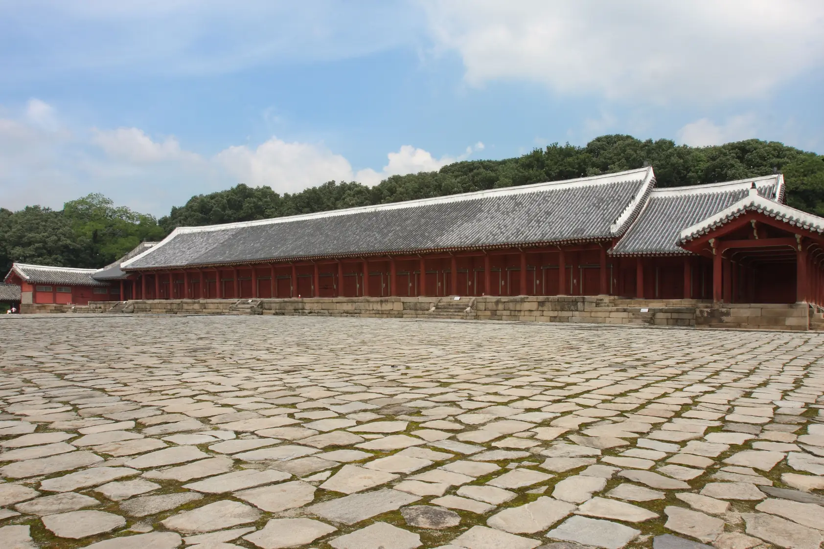 A long tiled-roof hall on a raised platform above a wide courtyard of rough stone slabs