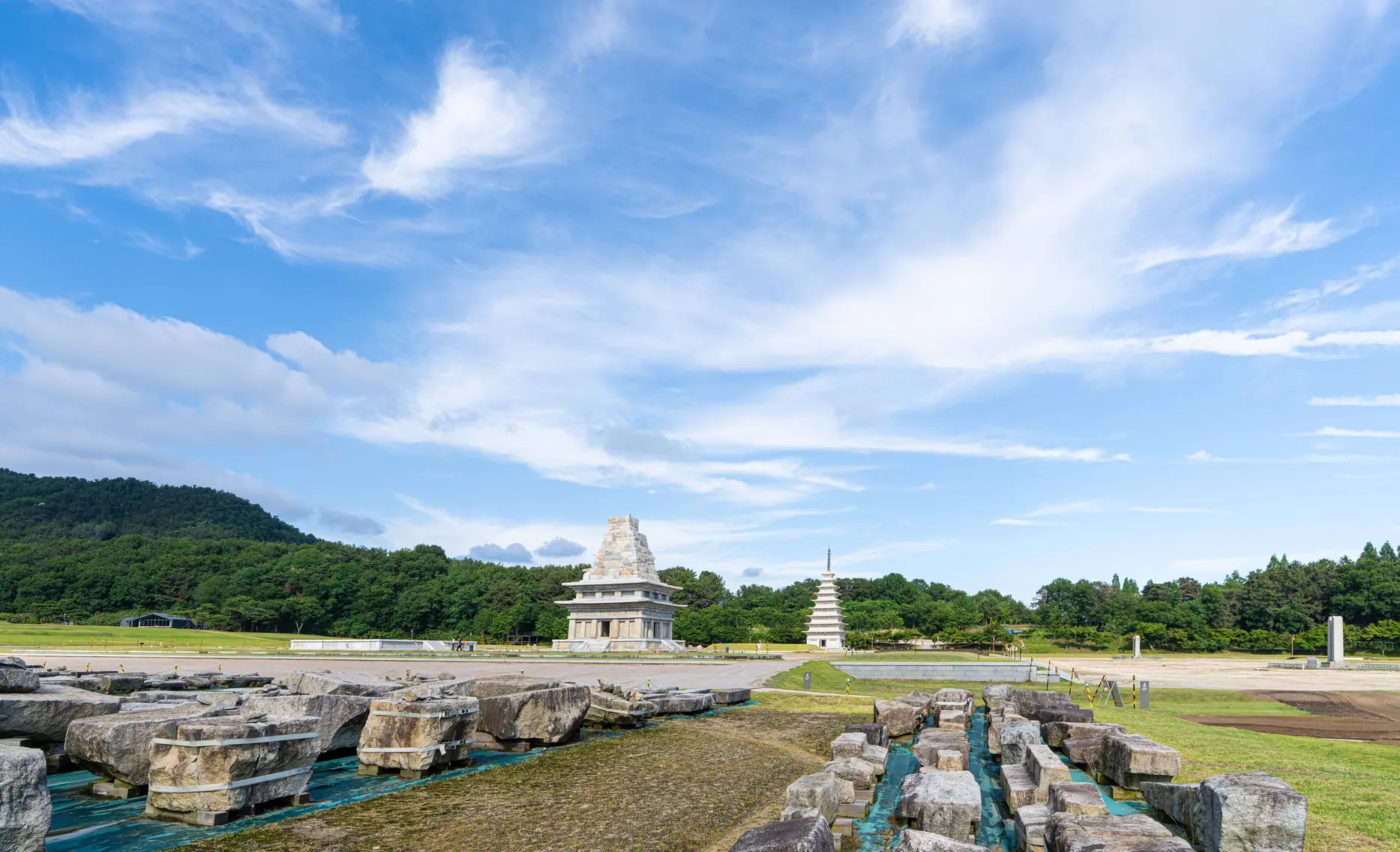 Two pagodas across an open archaeological site scattered with cut stone blocks